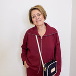 Person wearing a burgundy tracksuit with a black and white bag against a white background