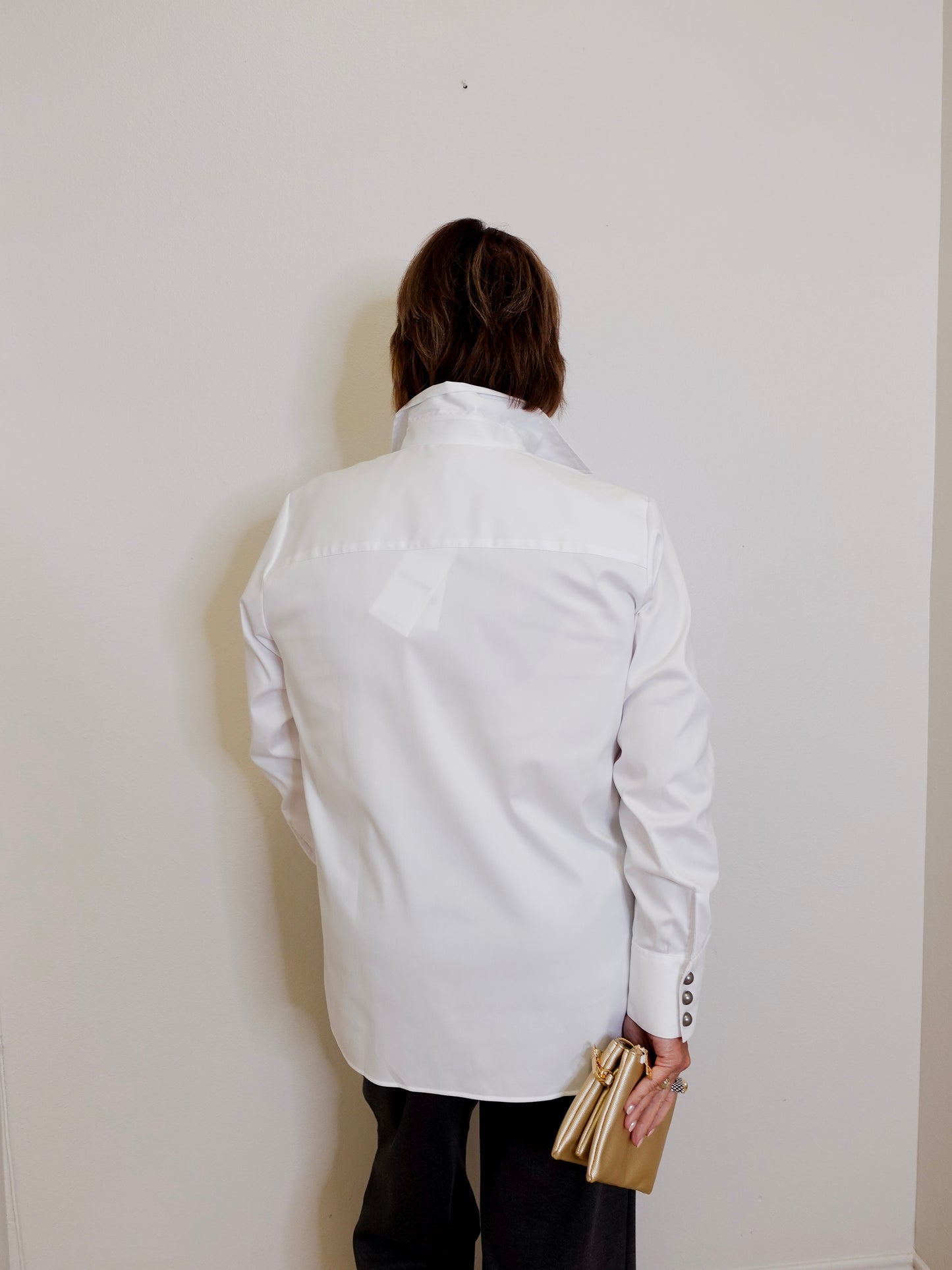 Person wearing a white jacket against a plain wall