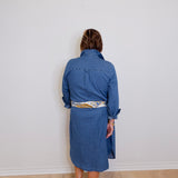 Person wearing a blue dress standing against a white wall.