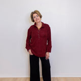 Woman wearing a red shirt and black pants standing against a white wall.