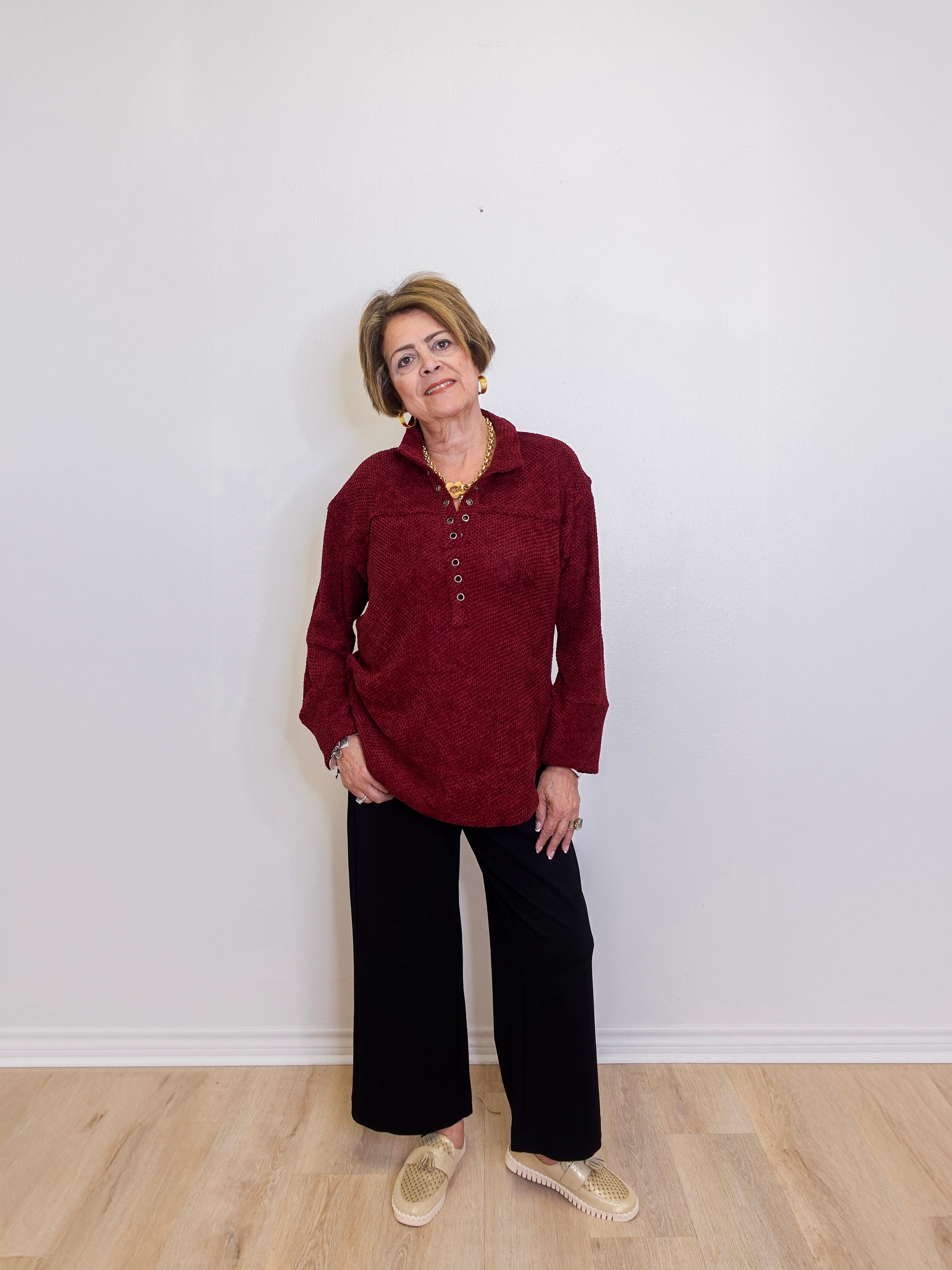 Woman wearing a red shirt and black pants standing against a white wall.