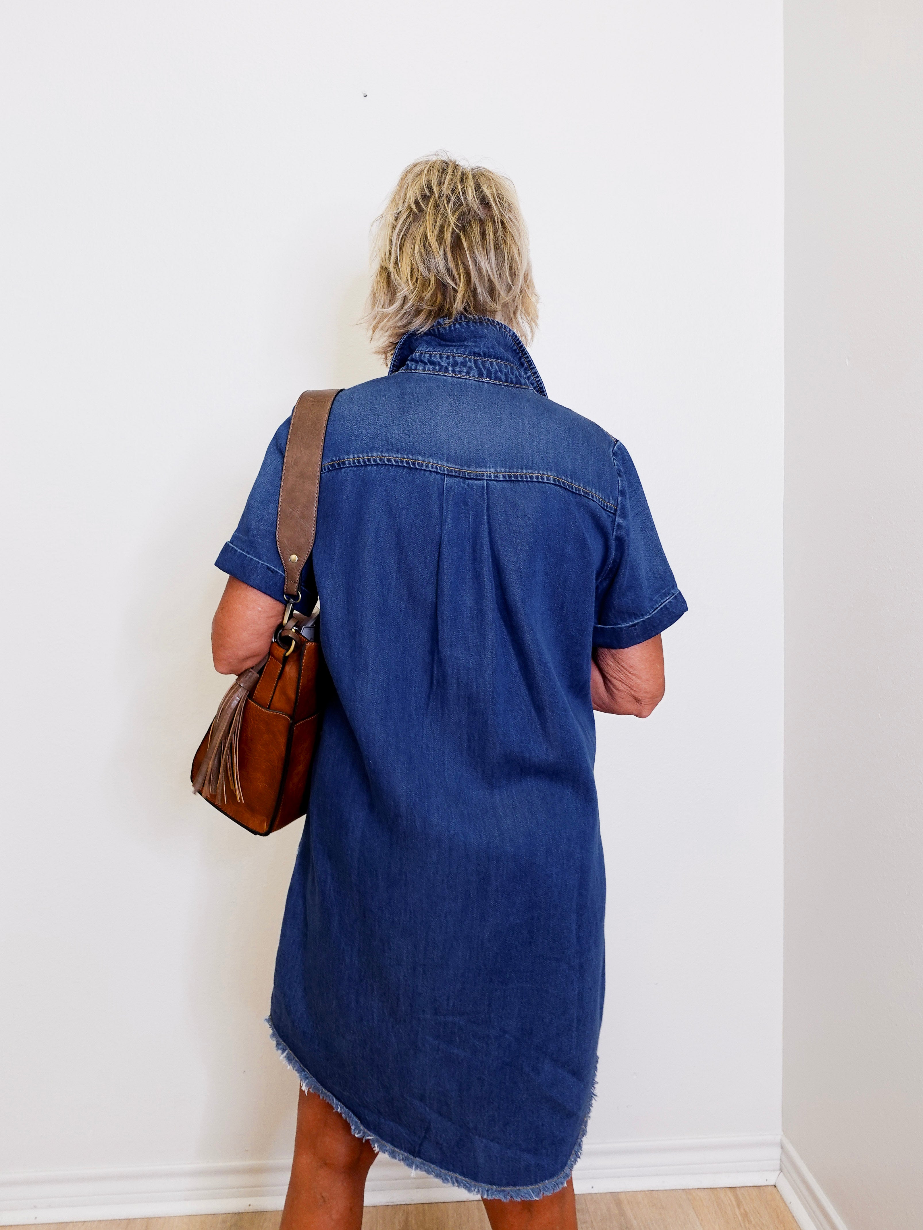 Woman wearing a blue popover shirt dress with pockets in front a white background.