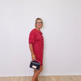 Woman in a red dress holding a blue handbag against a white wall.