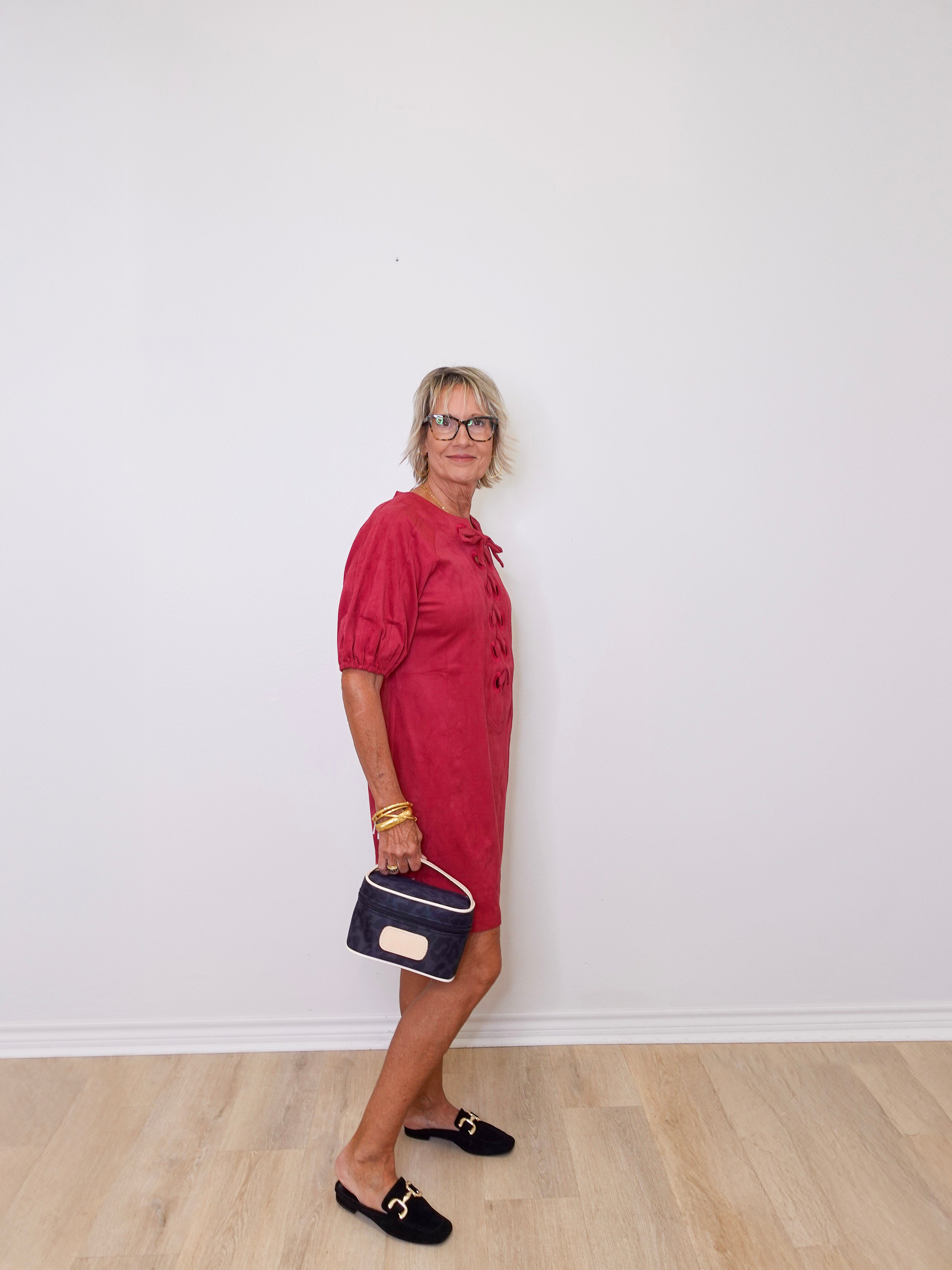 Woman in a red dress holding a blue handbag against a white wall.
