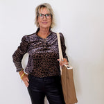 Woman wearing a leopard print shirt and black pants, holding a beige bag against a white background