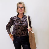 Woman wearing a leopard print shirt and black pants, holding a beige bag against a white background