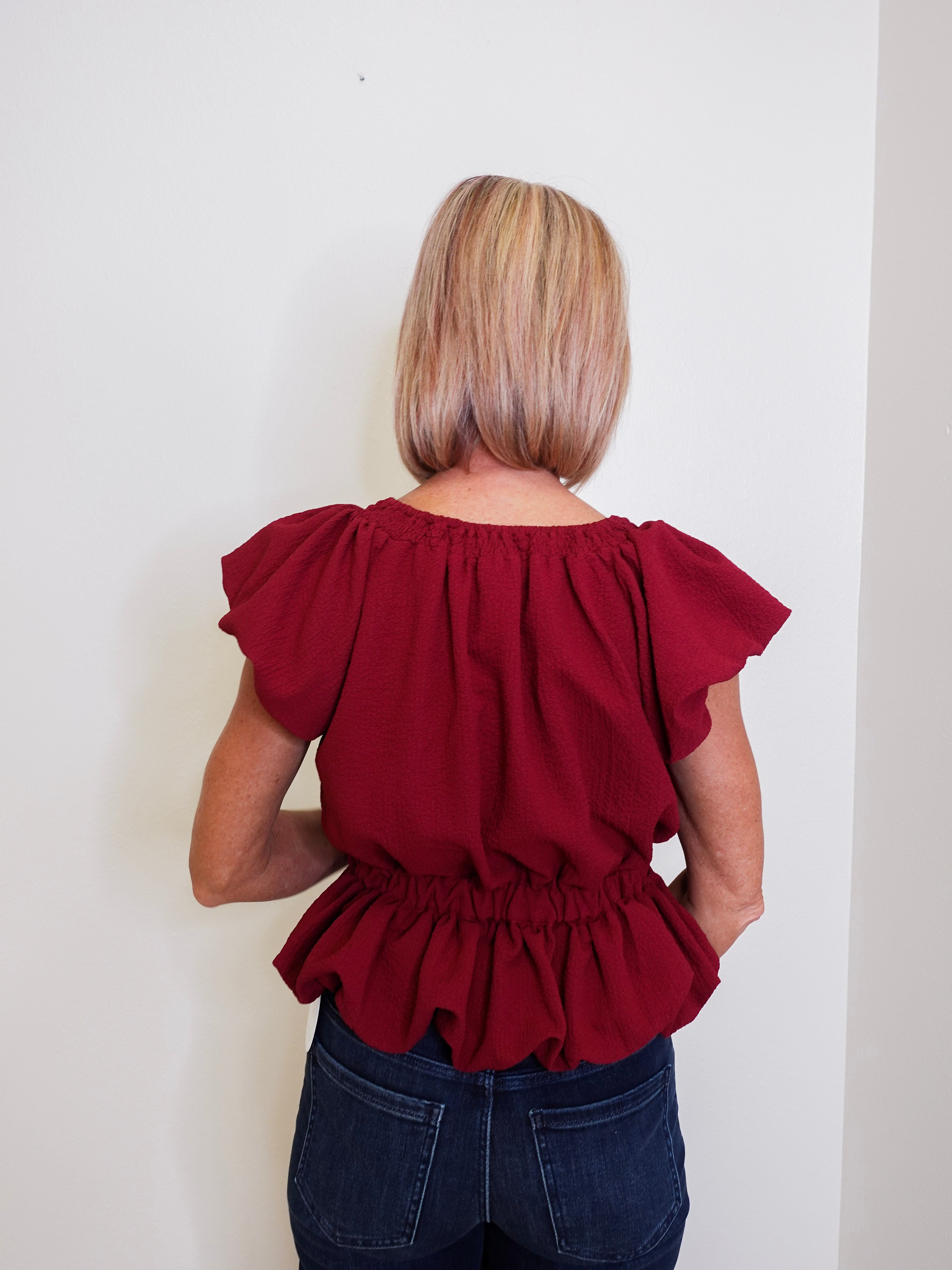 Person wearing a red blouse with ruffled sleeves against a white background