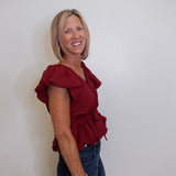 Woman wearing a red blouse and blue jeans against a white wall