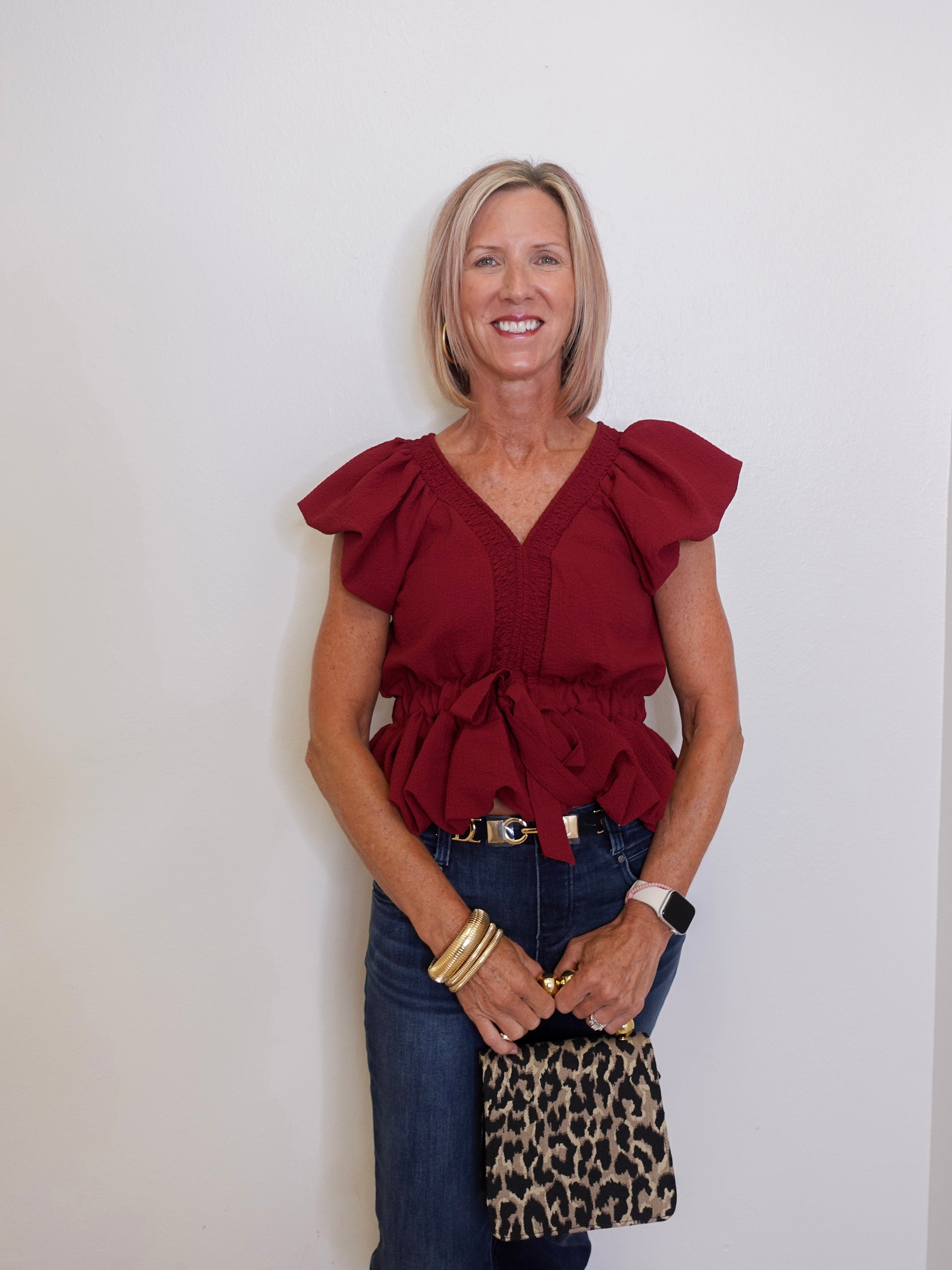 Woman wearing a red blouse and blue jeans, holding a leopard print bag against a white background