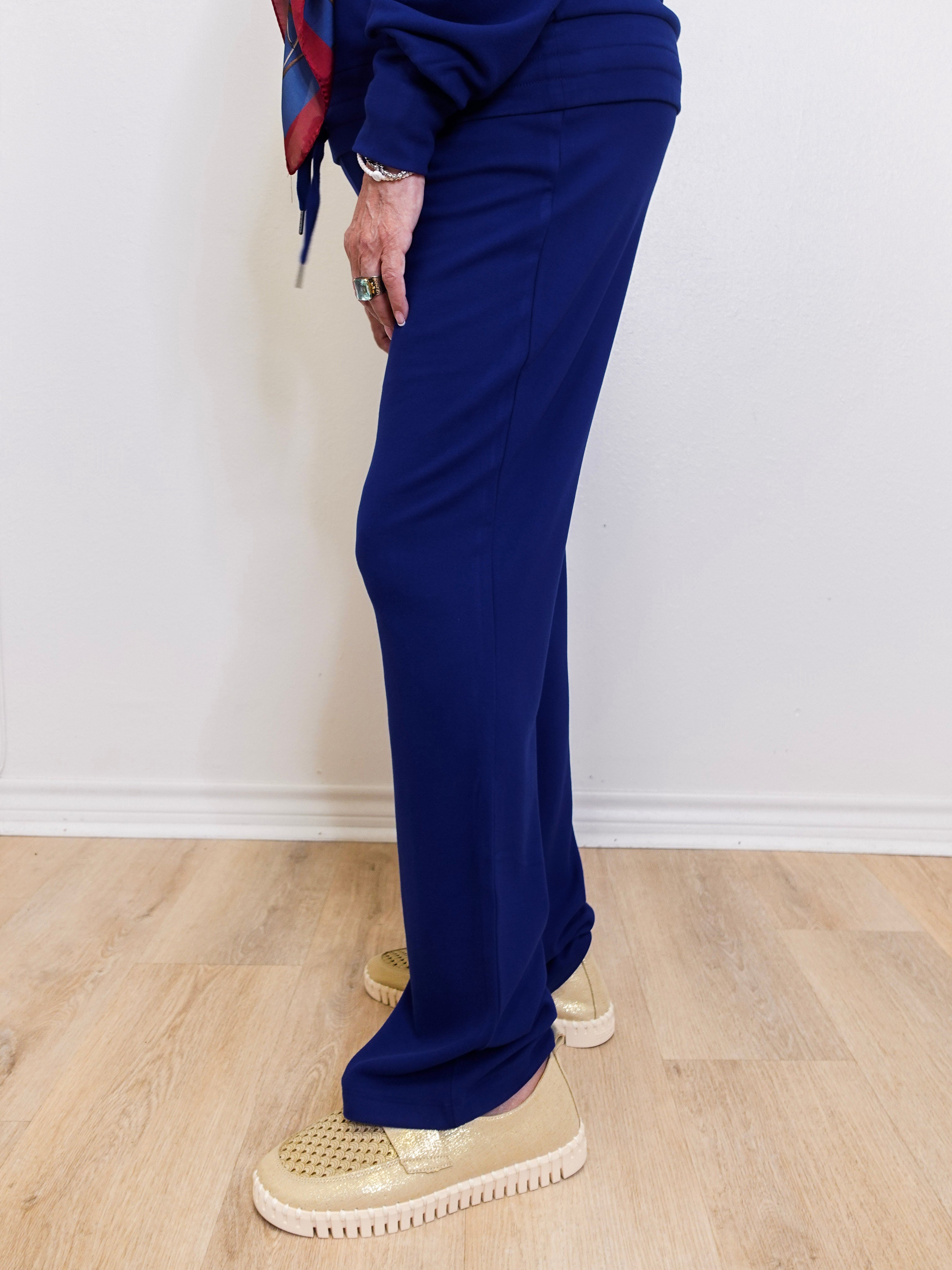 Person wearing a blue outfit with a patterned scarf against a white wall.