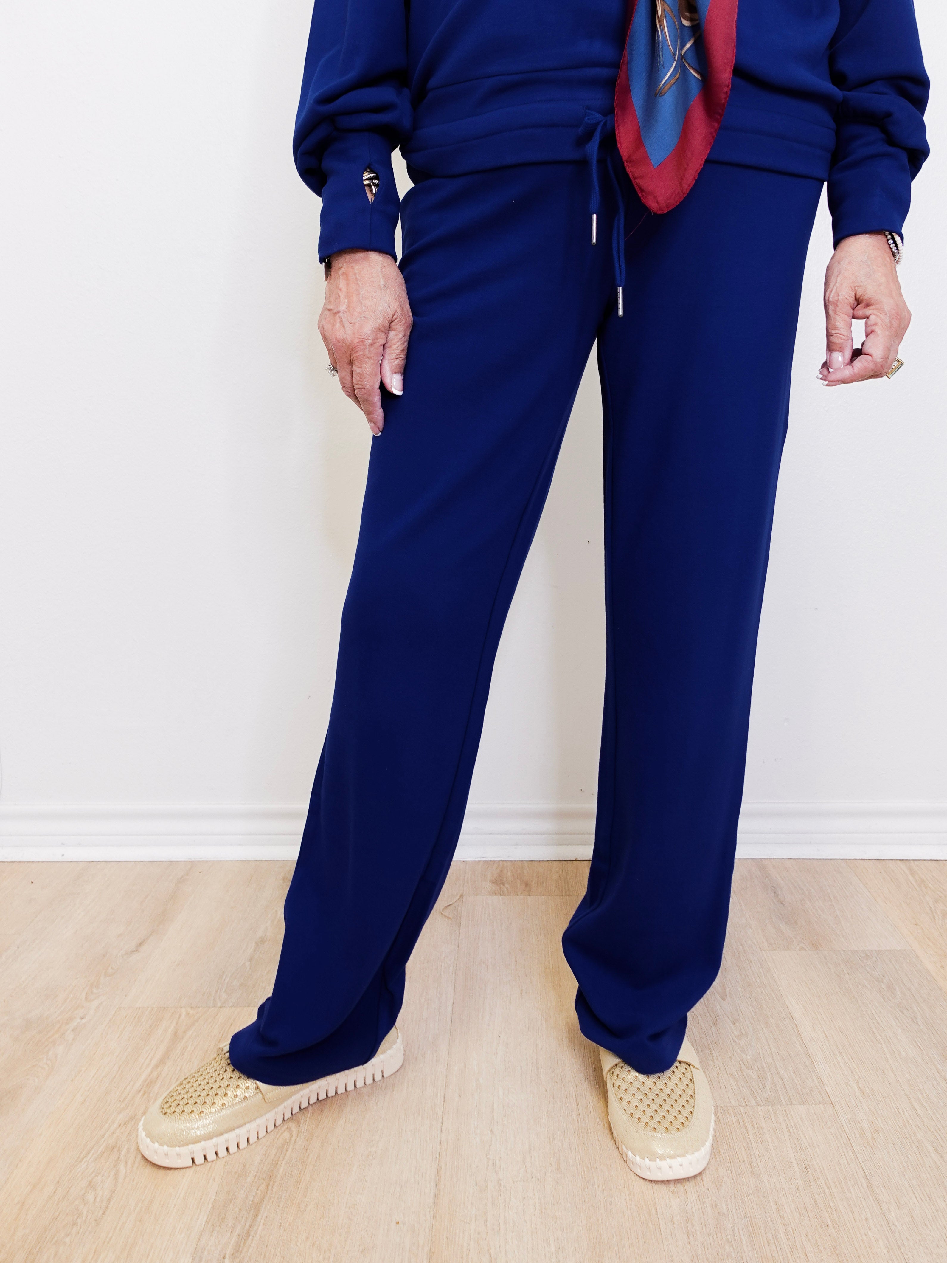 Person wearing a blue outfit with a patterned scarf against a white wall.