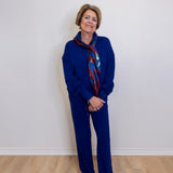 Person wearing a blue outfit with a patterned scarf against a white wall.