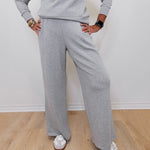 Person wearing a gray sweatshirt and pants with white sneakers on a wooden floor.