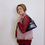 Woman wearing a red shirt and patterned vest, holding a black handbag against a white background