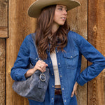 Woman wearing a blue denim jacket and beige cowboy hat, holding a gray bag against a wooden background