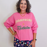Woman wearing a pink sweatshirt with 'Champagne & Mistletoe' text and patterned shorts on a white background