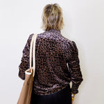 Person wearing a leopard print jacket holding a beige bag against a white background