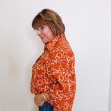 Woman wearing an orange patterned blouse against a white background