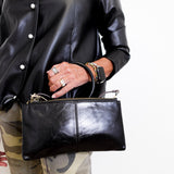 Person wearing a black leather jacket and holding a matching black leather clutch.