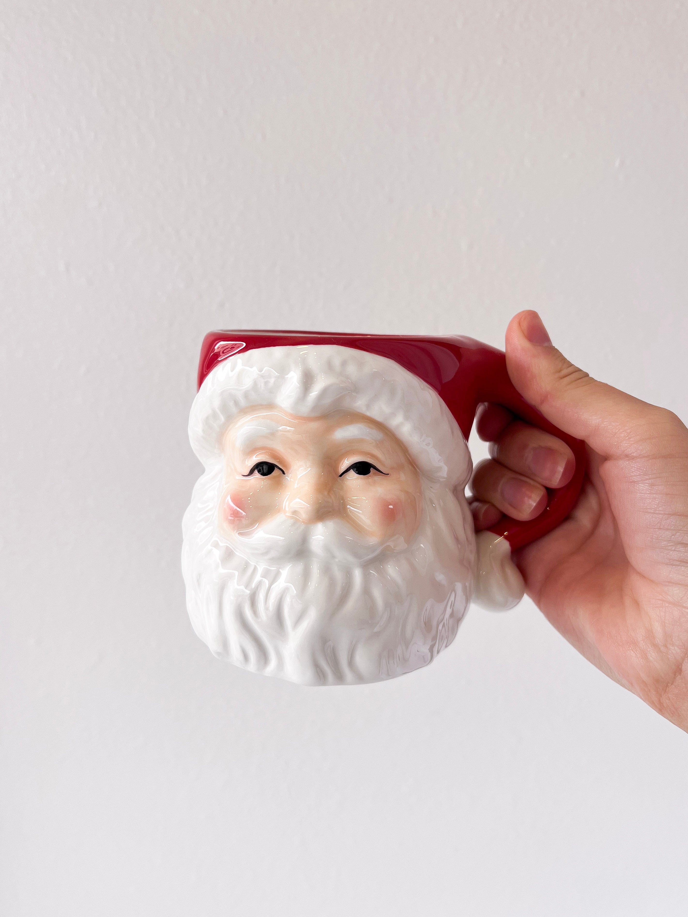Hand holding a ceramic mug shaped like a Santa Claus face against a plain background