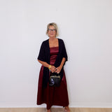 Woman wearing a dark red dress and black cardigan against a white wall.