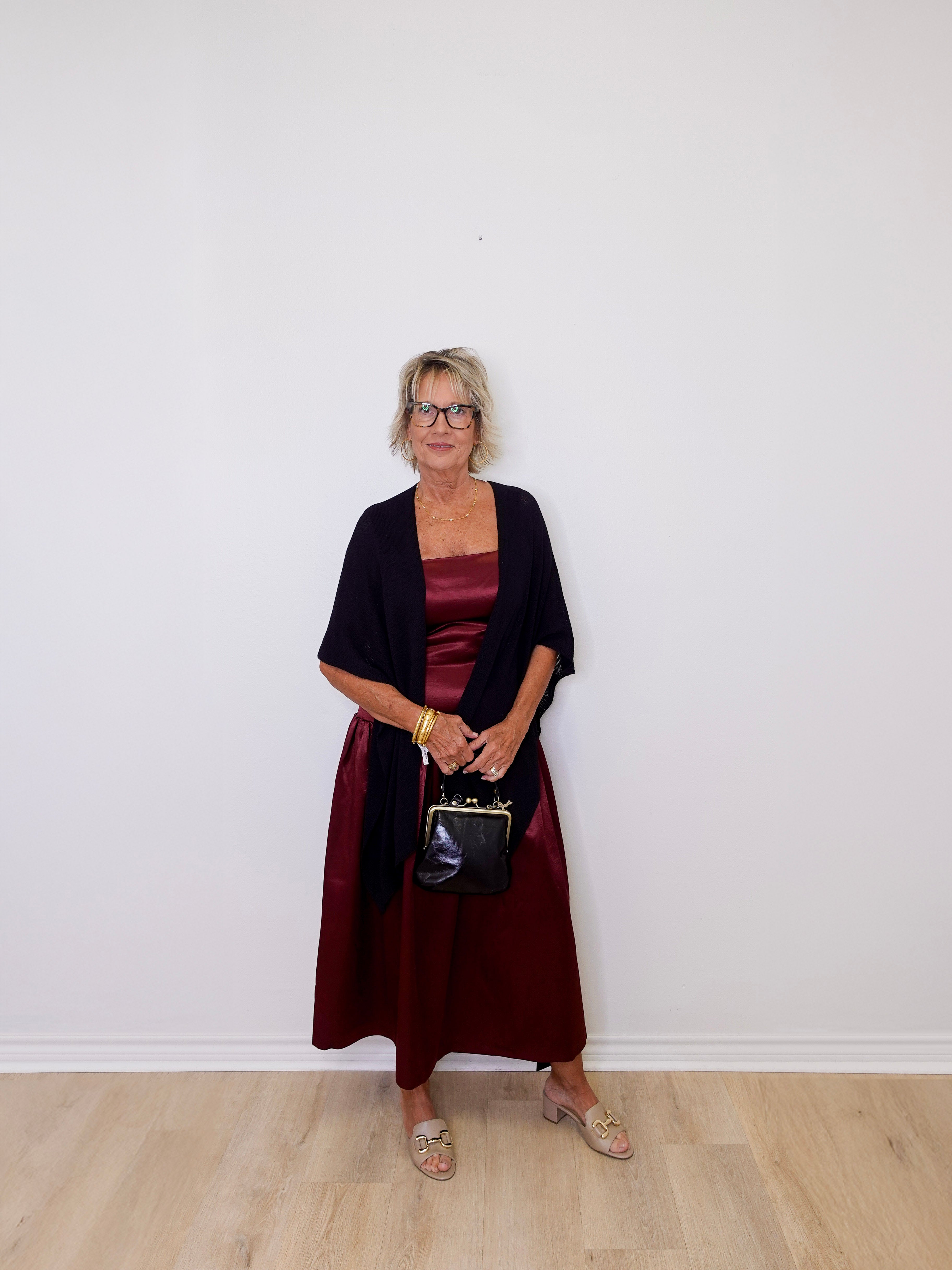 Woman wearing a dark red dress and black cardigan against a white wall.
