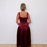 Person wearing a burgundy satin dress against a white wall.