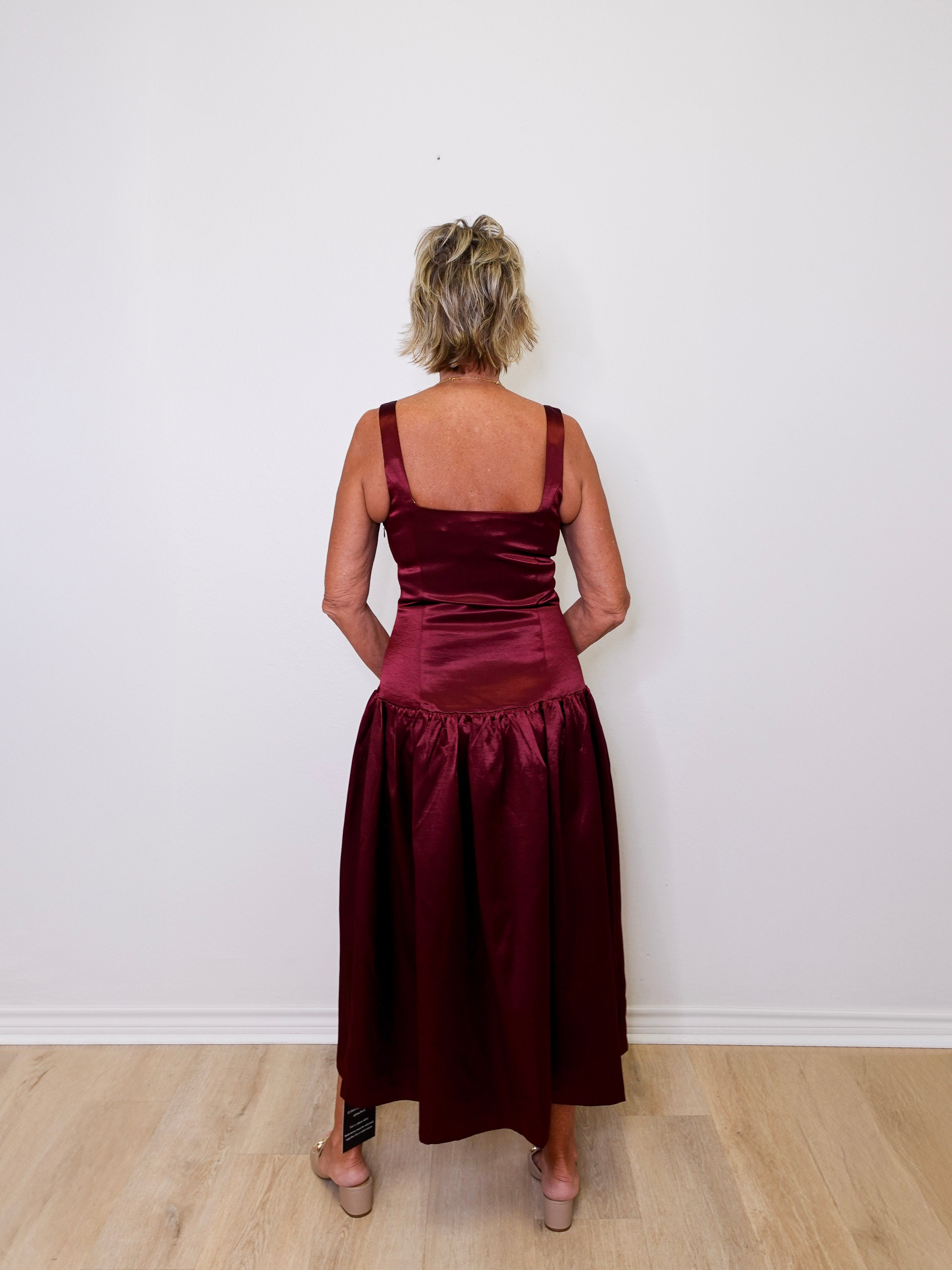 Person wearing a burgundy satin dress against a white wall.