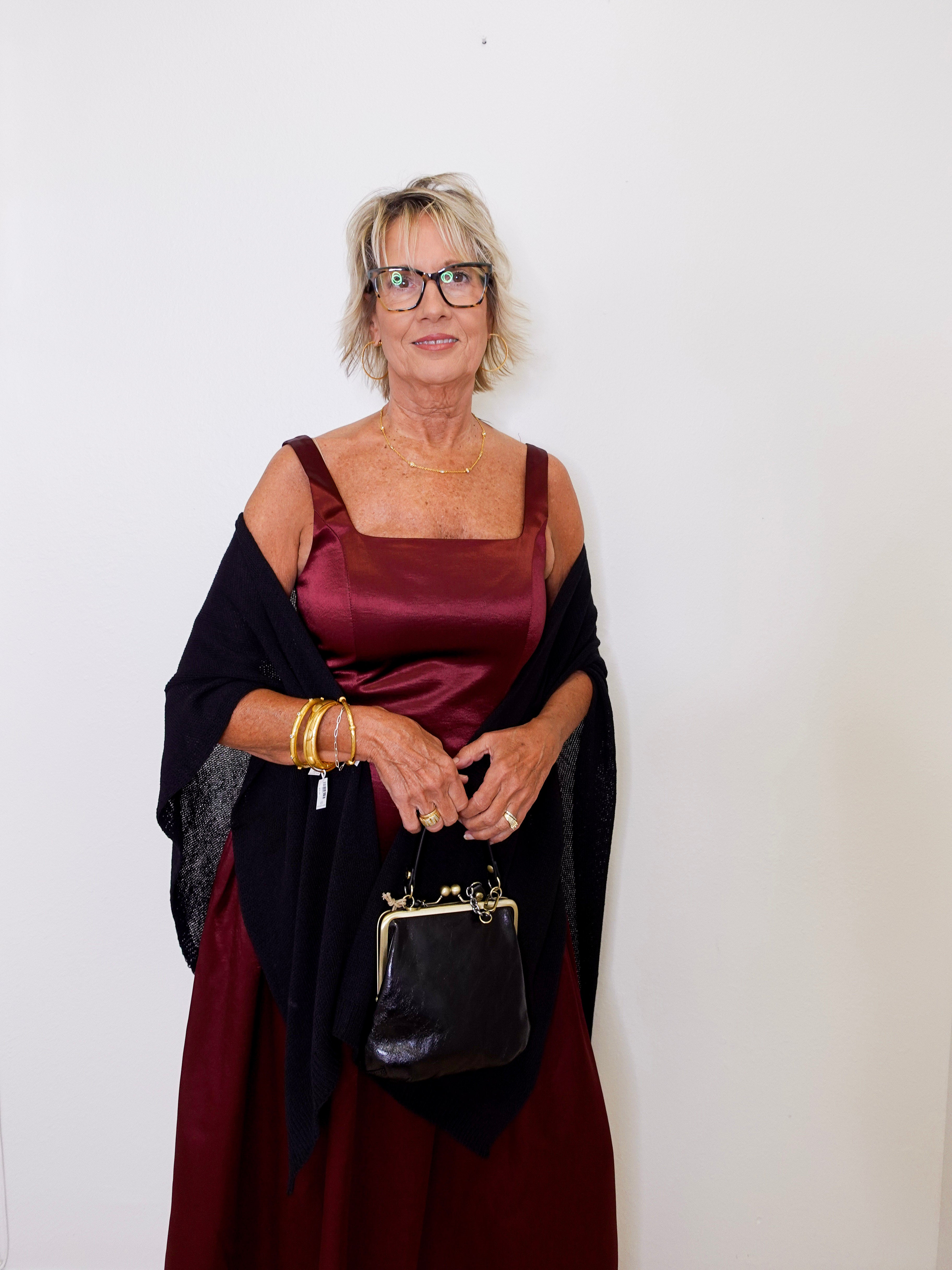 Woman wearing a burgundy dress with a black shawl and holding a black handbag against a white background
