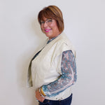 Person wearing a cream jacket with lace sleeves against a white background