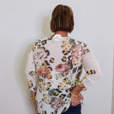 Person wearing a floral and leopard print top against a white wall