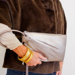 Person holding a silver clutch with a plain background