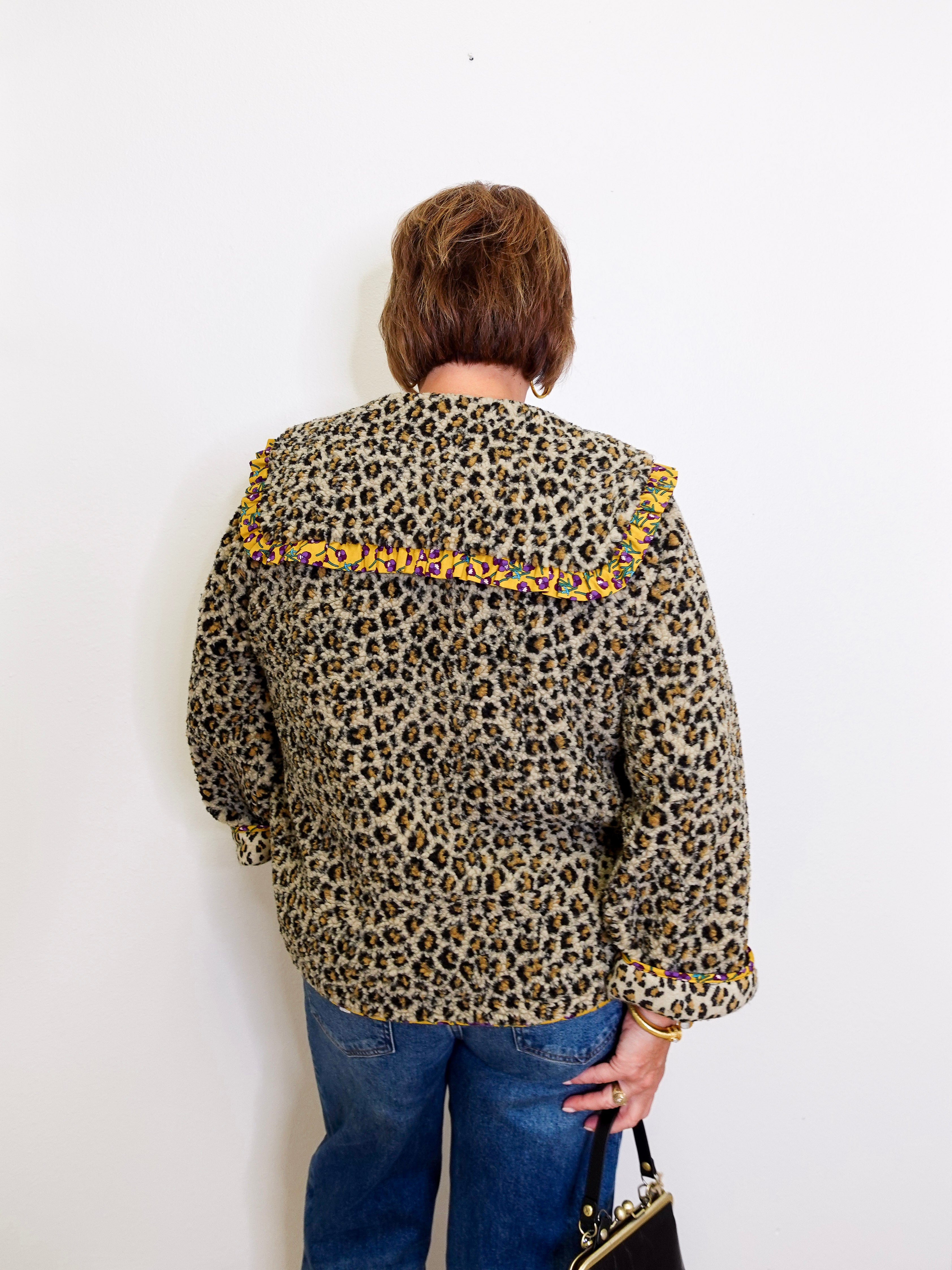 Person wearing a leopard print jacket with yellow accents on a white background