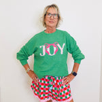 Person wearing a green 'JOY' sweater and checkered shorts against a white background