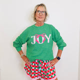 Person wearing a green 'JOY' sweater and checkered shorts against a white background