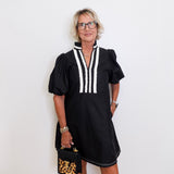Woman wearing a black dress with white accents against a white wall