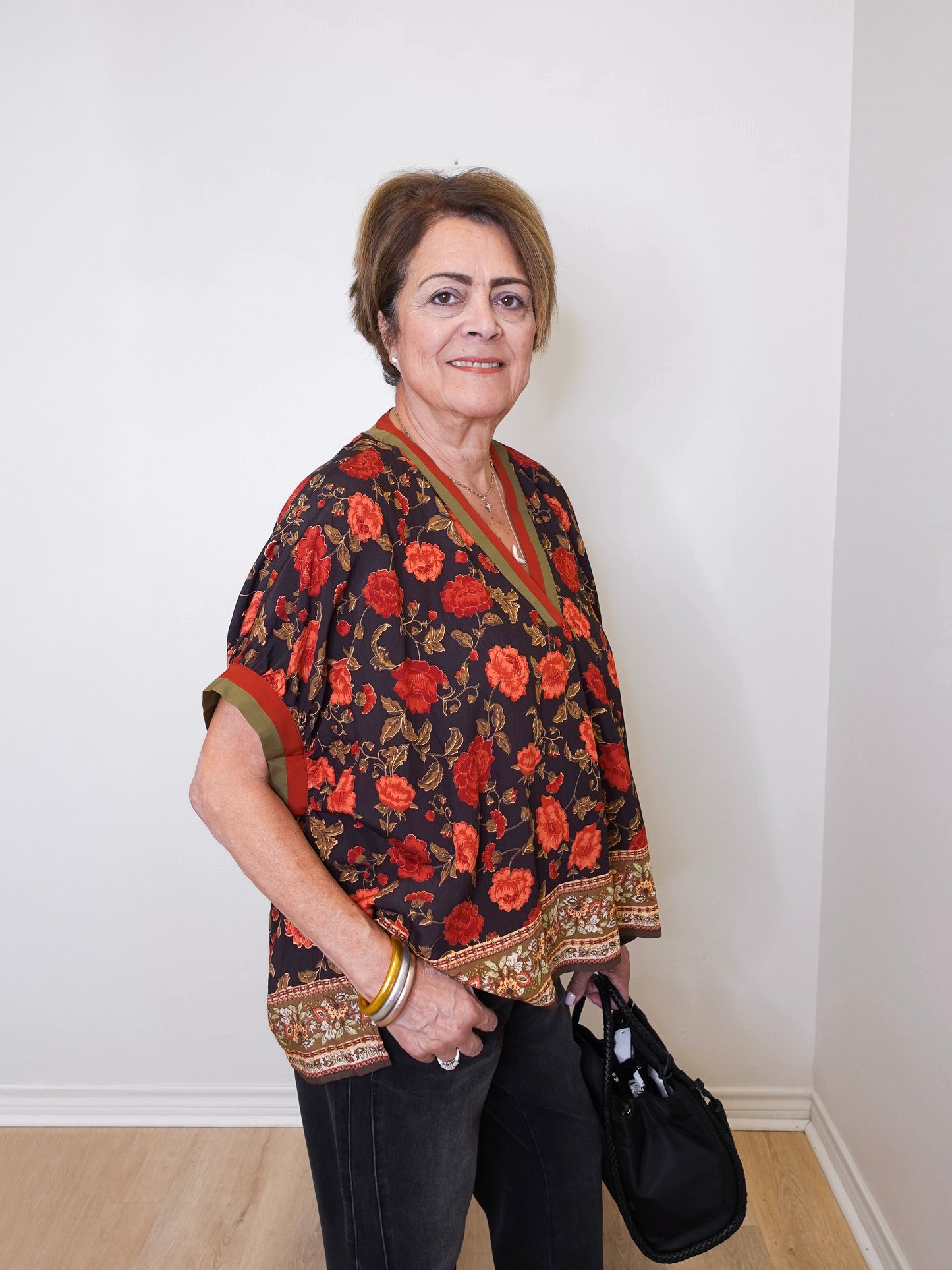 a women wearing a black short sleeve floral print top with black pants, on a white background