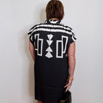 Person wearing a black dress with white geometric patterns against a white wall.