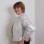 Person wearing a silver jacket against a white wall