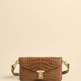 Brown crocodile-patterned handbag with gold hardware on a beige background