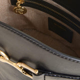 Close-up of a gray handbag with gold zipper and handle, featuring a brand logo.