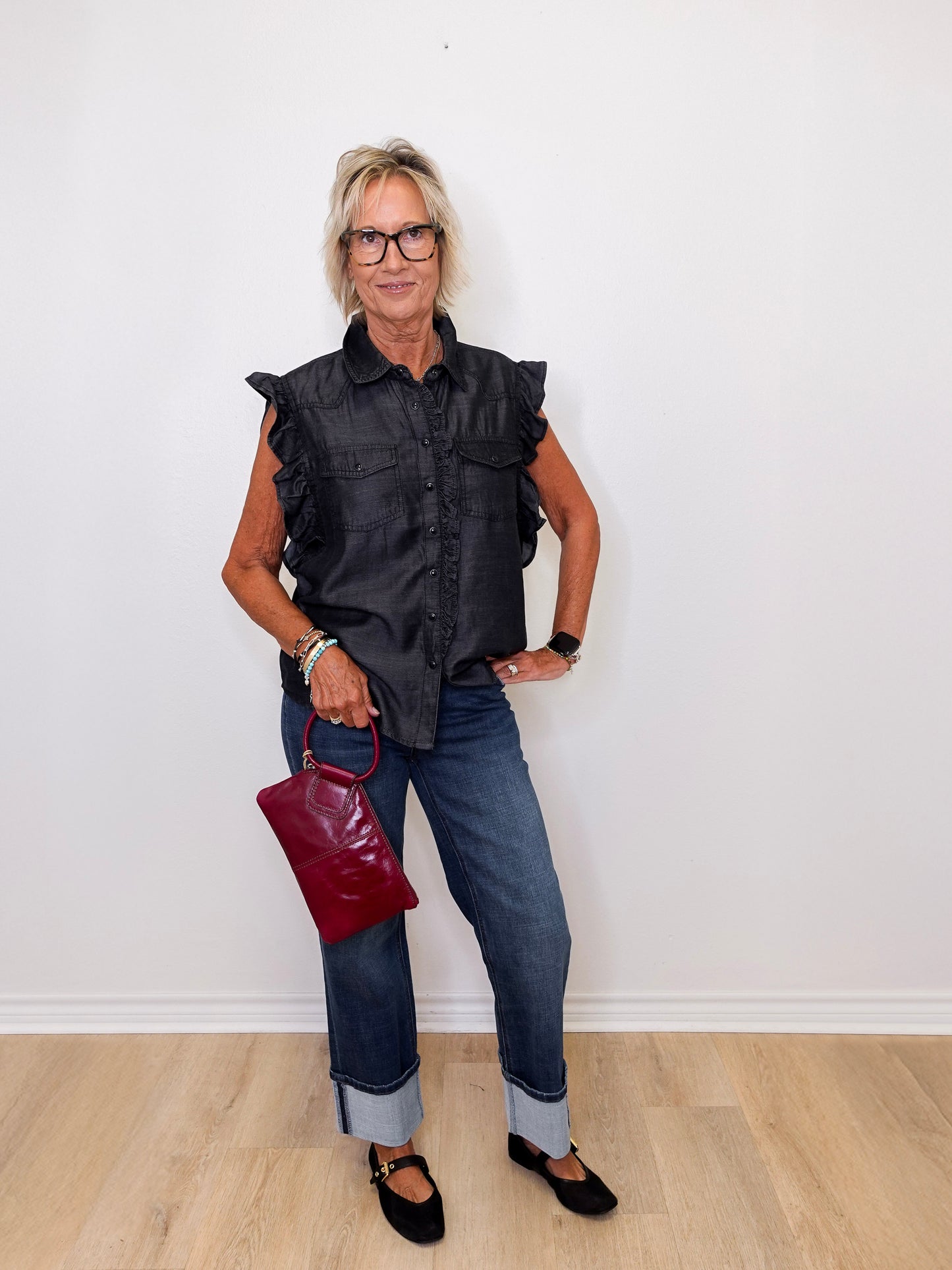 Woman wearing a black sleeveless shirt, blue jeans, and holding a red handbag against a white background