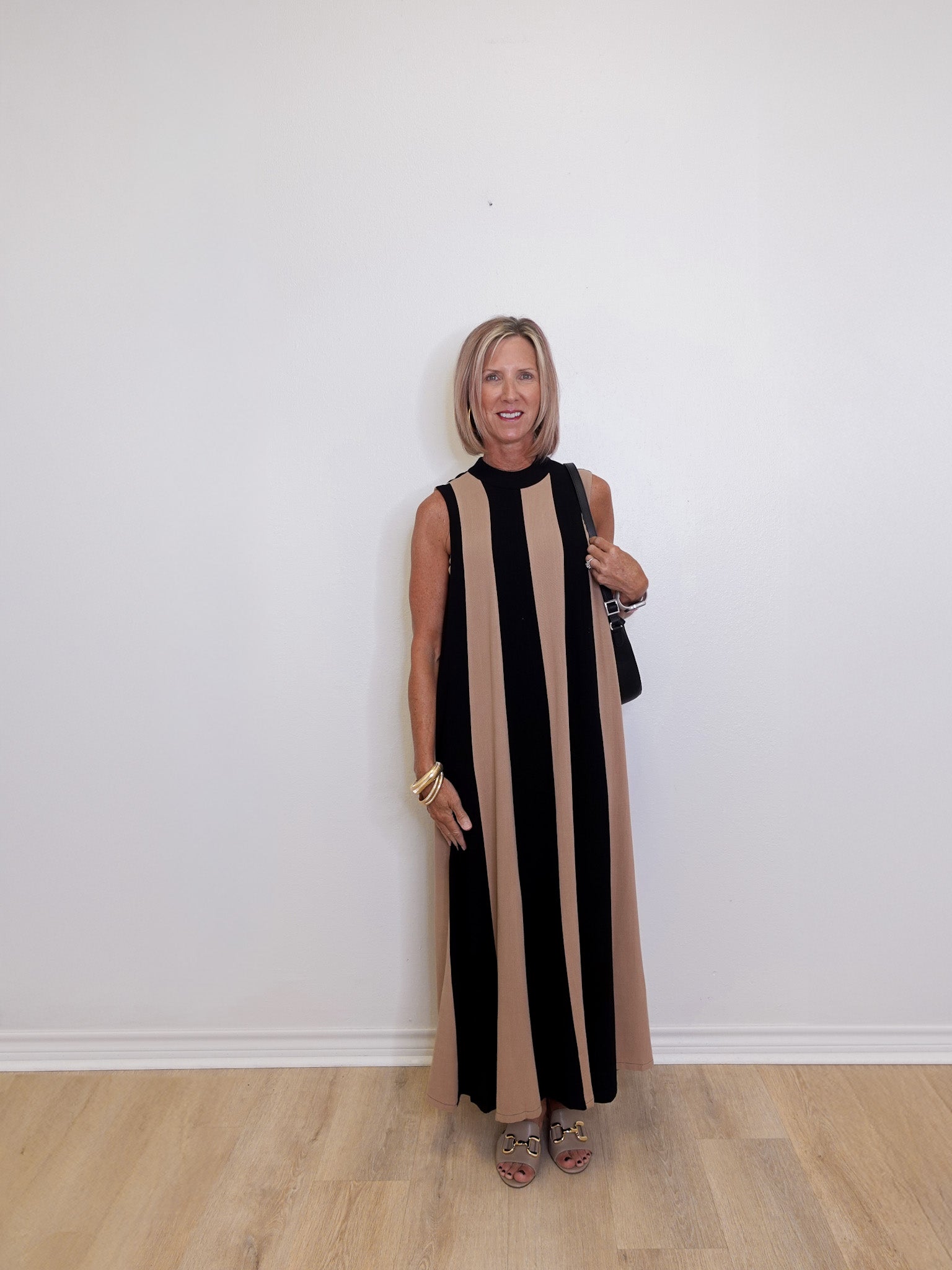 woman wearing a Black and taupe stripe sleeveless maxi dress for special events against a white background.