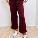 Person wearing a burgundy outfit with white sneakers on a light wooden floor.