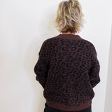 Person wearing a brown leopard print sweater against a white wall