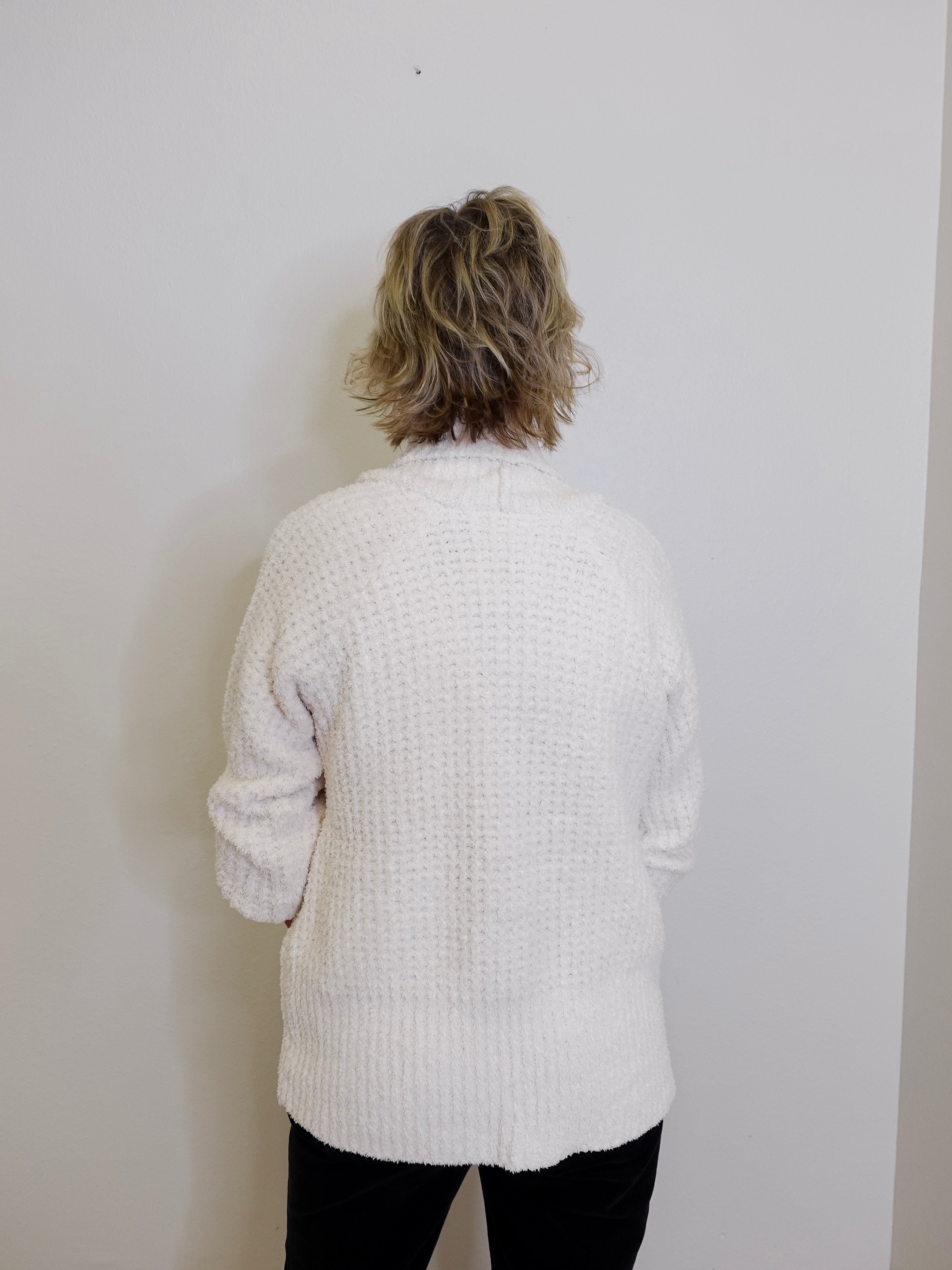 Person wearing a white textured sweater against a plain white background