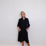 Person wearing a black dress standing against a white wall.