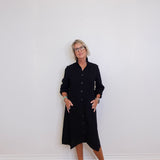 Person wearing a black dress standing against a white wall.