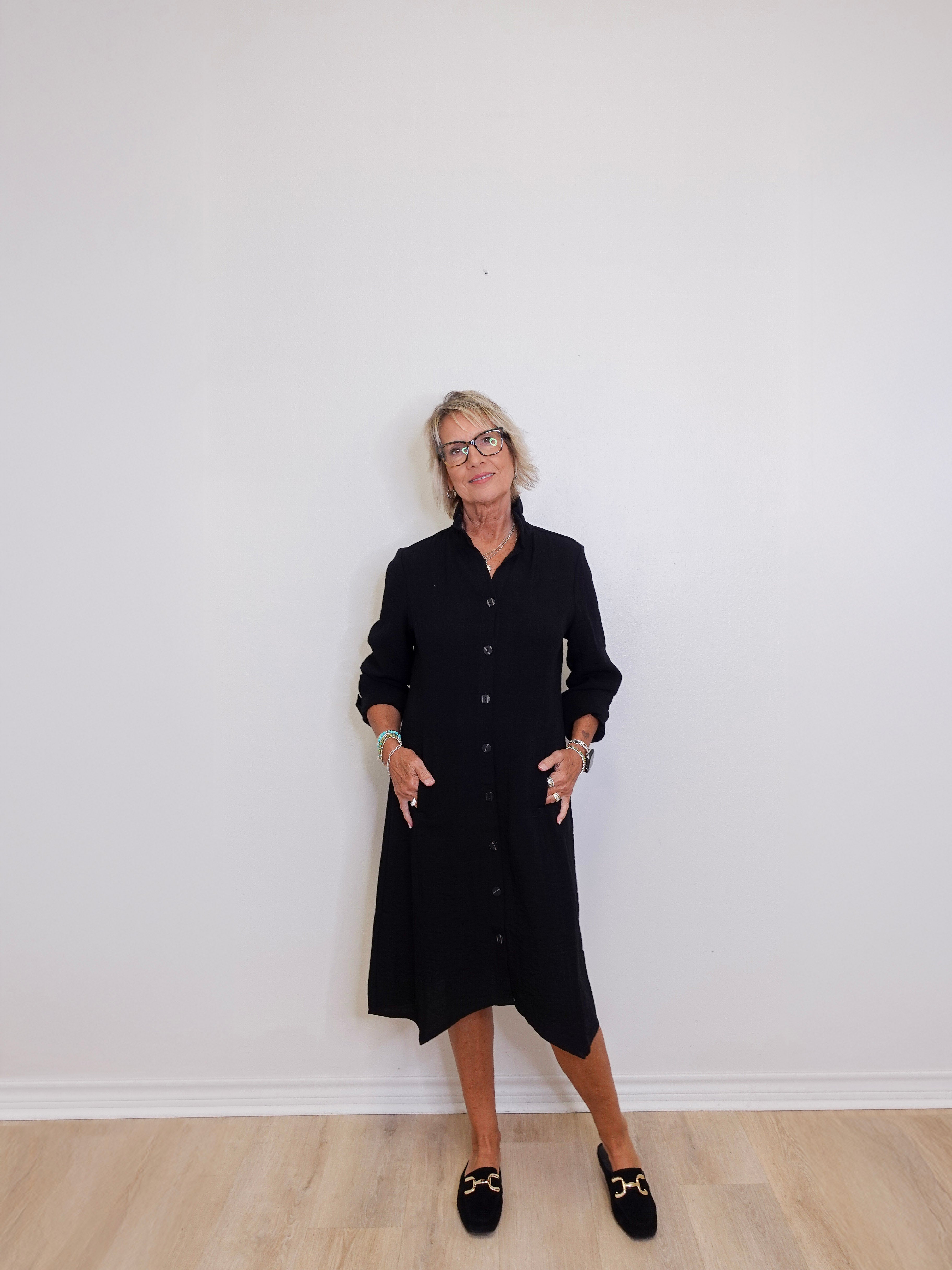 Person wearing a black dress standing against a white wall.