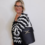 Woman wearing a black and white patterned sweater holding a black handbag against a plain background
